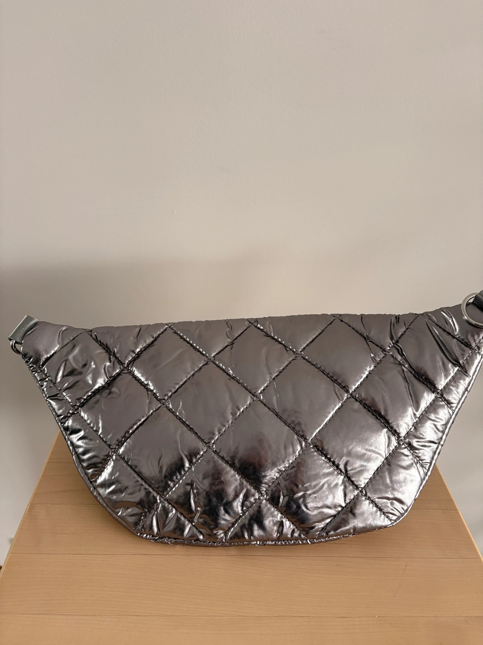 Sac banane XL matelassé effet doudoune argenté métallisé, grand format, posé sur une surface en bois