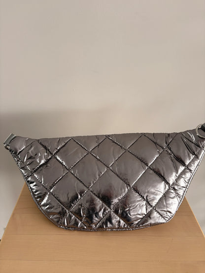 Sac banane XL matelassé effet doudoune argenté métallisé, grand format, posé sur une surface en bois