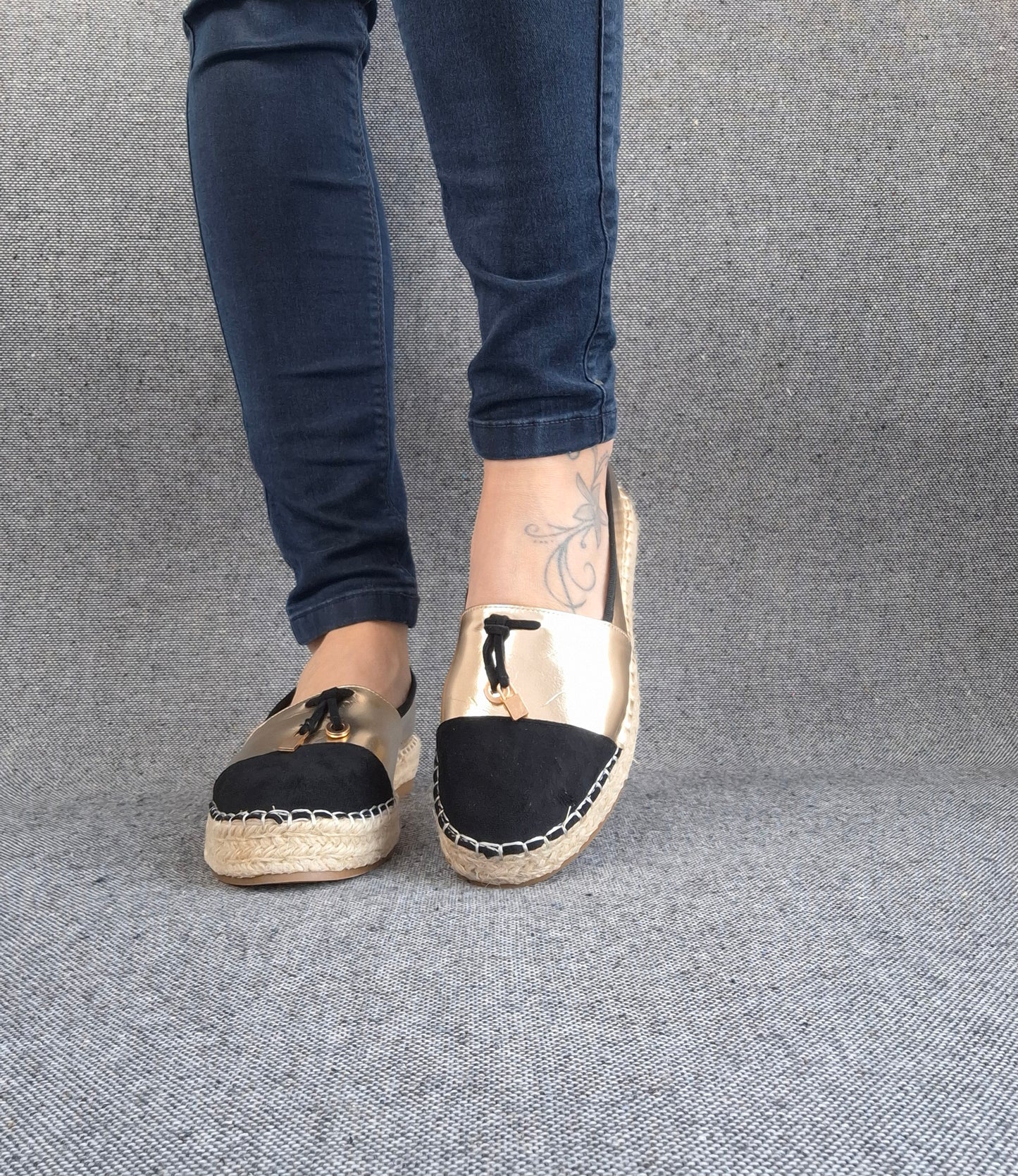 Espadrilles plates bicolore or et noir portées avec un jean, semelle tressée en jute et bout noir