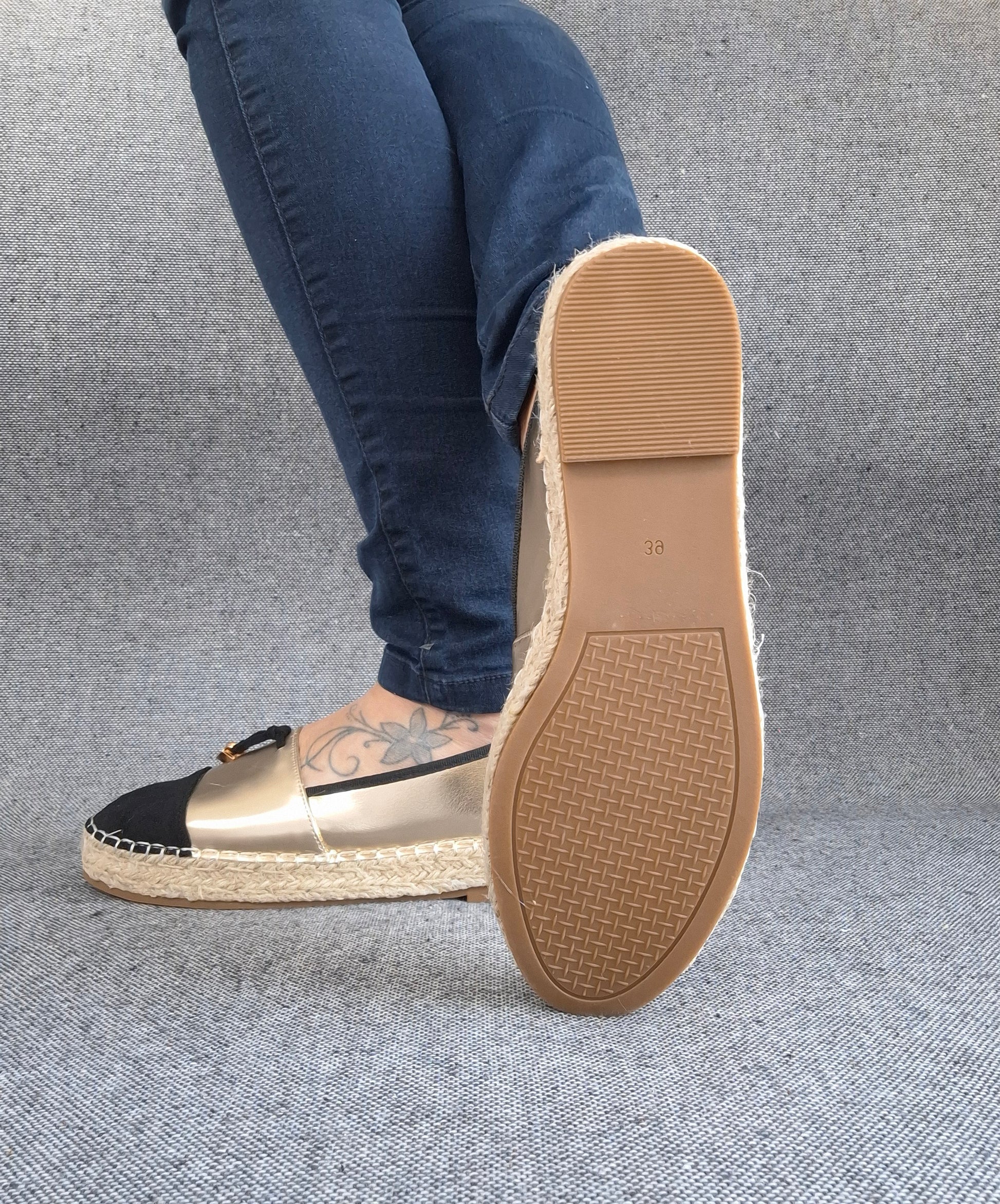 Semelle d'espadrilles plates bicolore or/noir avec tresse de jute, portées avec un jean bleu