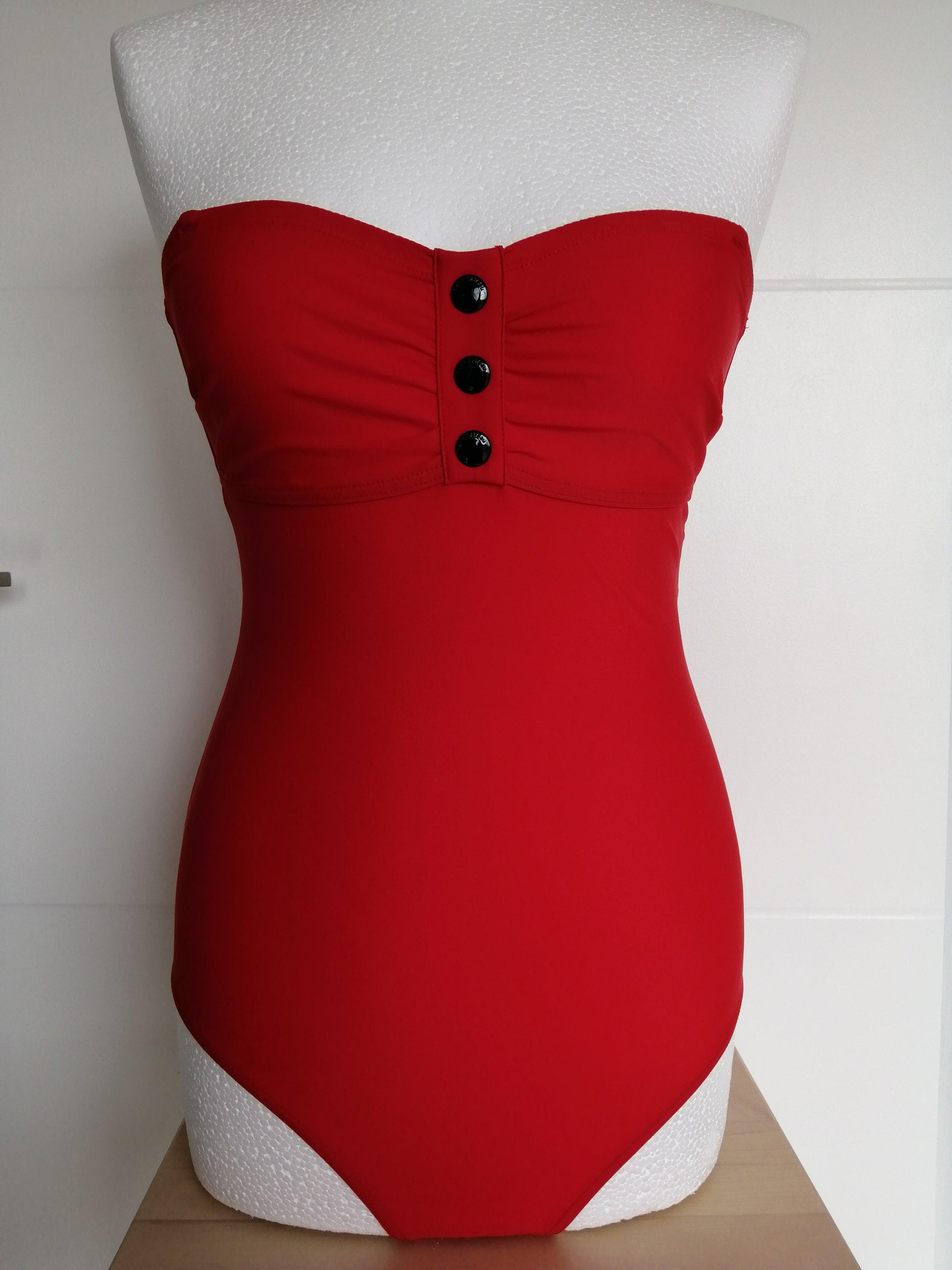 Red one-piece swimsuit with bustier top and black buttons, displayed on mannequin