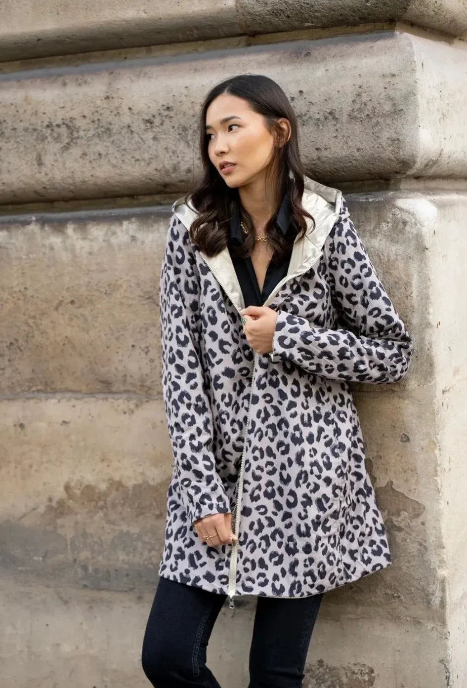 Imperméable réversible long léopard Laura Jo côté imprimé animal, doublure dorée visible, porté par une femme adossée à un mur en pierre