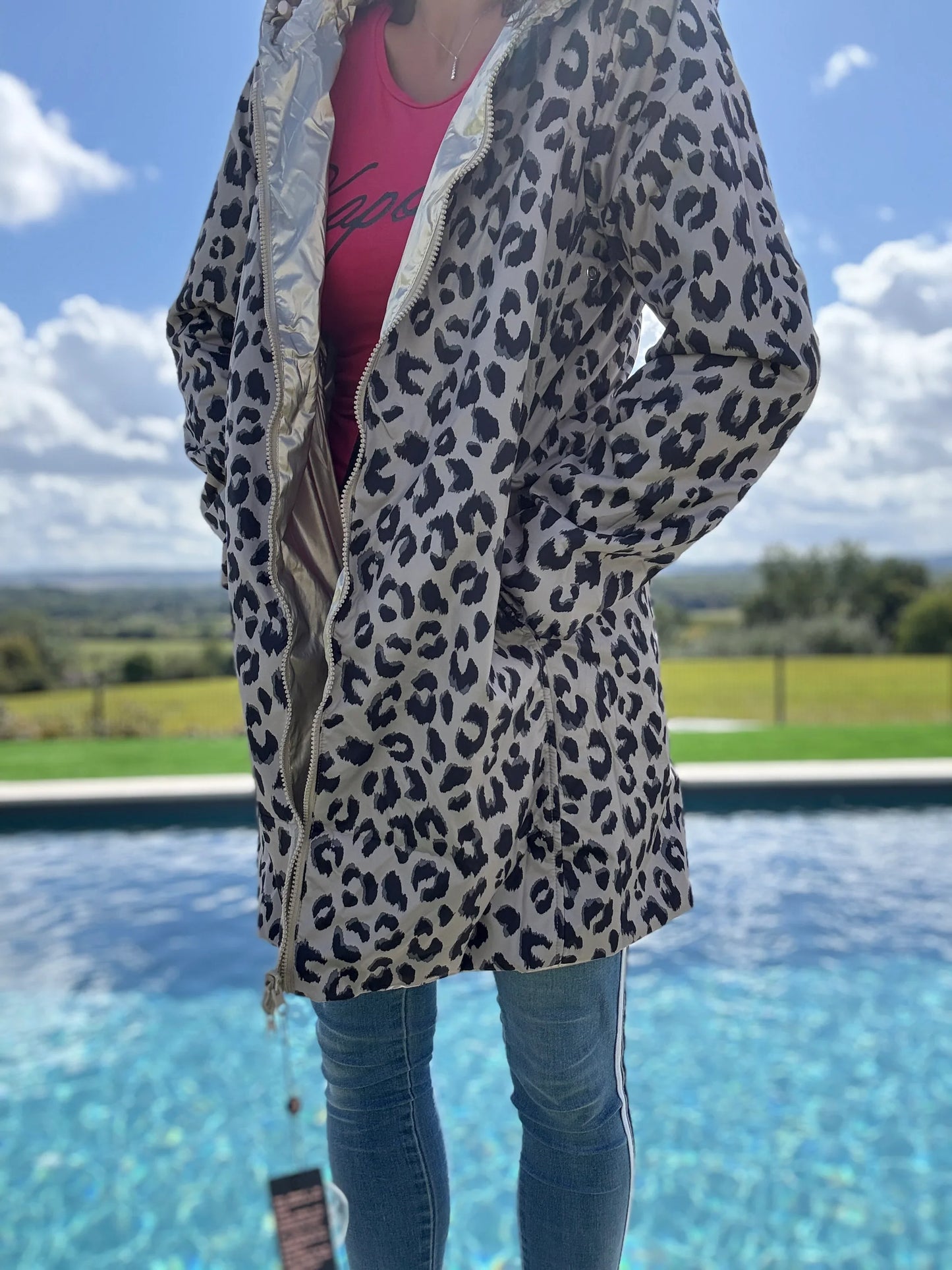 Imperméable réversible long léopard Laura Jo ouvert, révélant doublure dorée, porté avec jean et t-shirt rose près d'une piscine