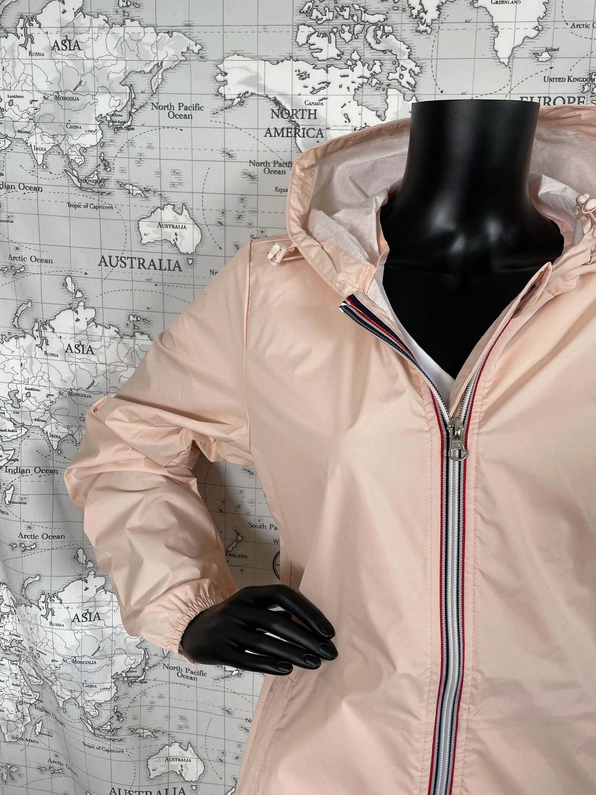 Laura Jo light pink raincoat with hood, displayed on mannequin, world map background