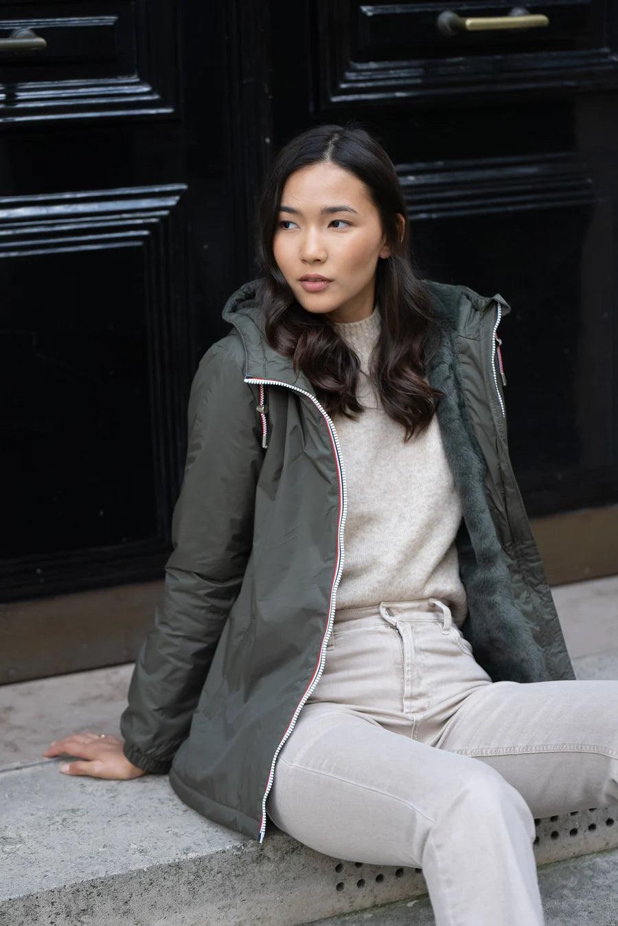 Woman wearing a khaki Laura Jo mid-length raincoat with faux fur and tricolor drawcord