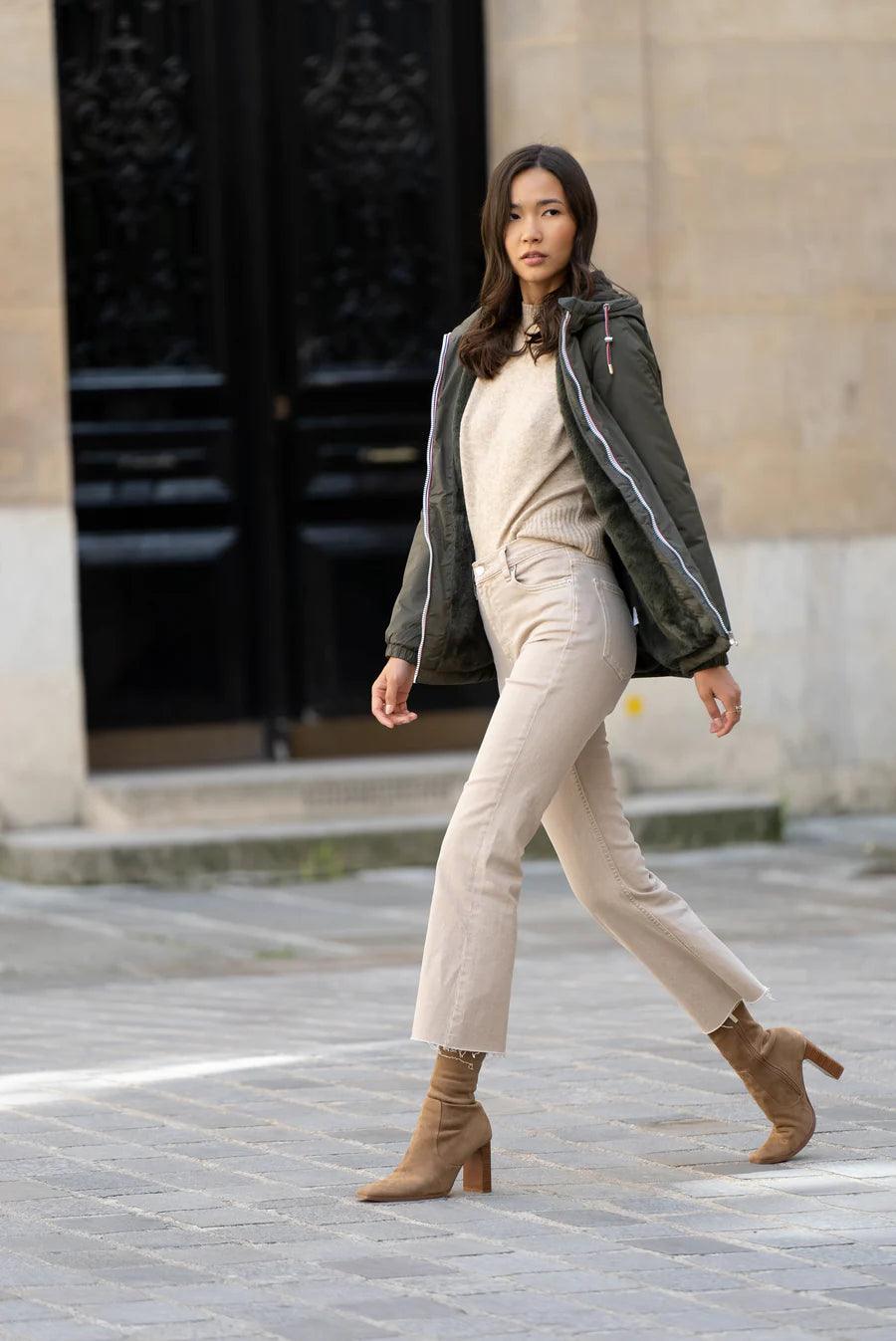 Woman wearing a khaki Laura Jo mid-length raincoat with faux fur and tricolor cord, walking outside