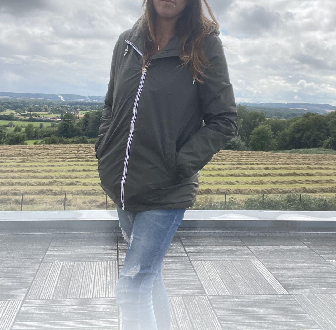 Woman in green Laura Jo raincoat and jeans outdoors on terrace with countryside view