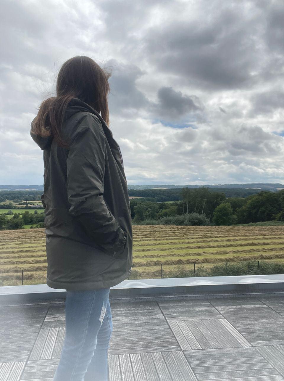 Woman in Laura Jo raincoat outdoors, standing on terrace with rural landscape view