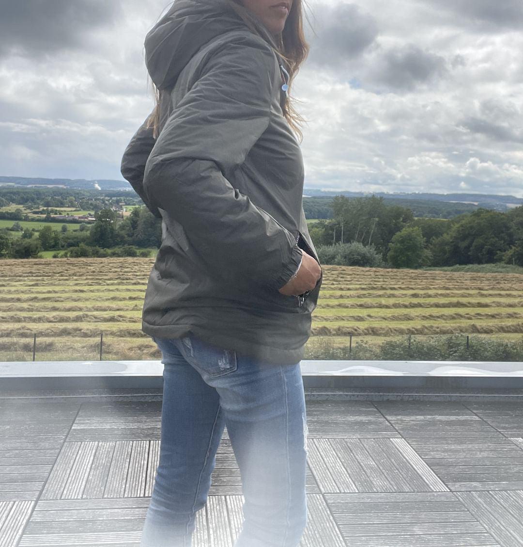 Woman wearing a Laura Jo rain jacket and jeans outdoors with scenic countryside view