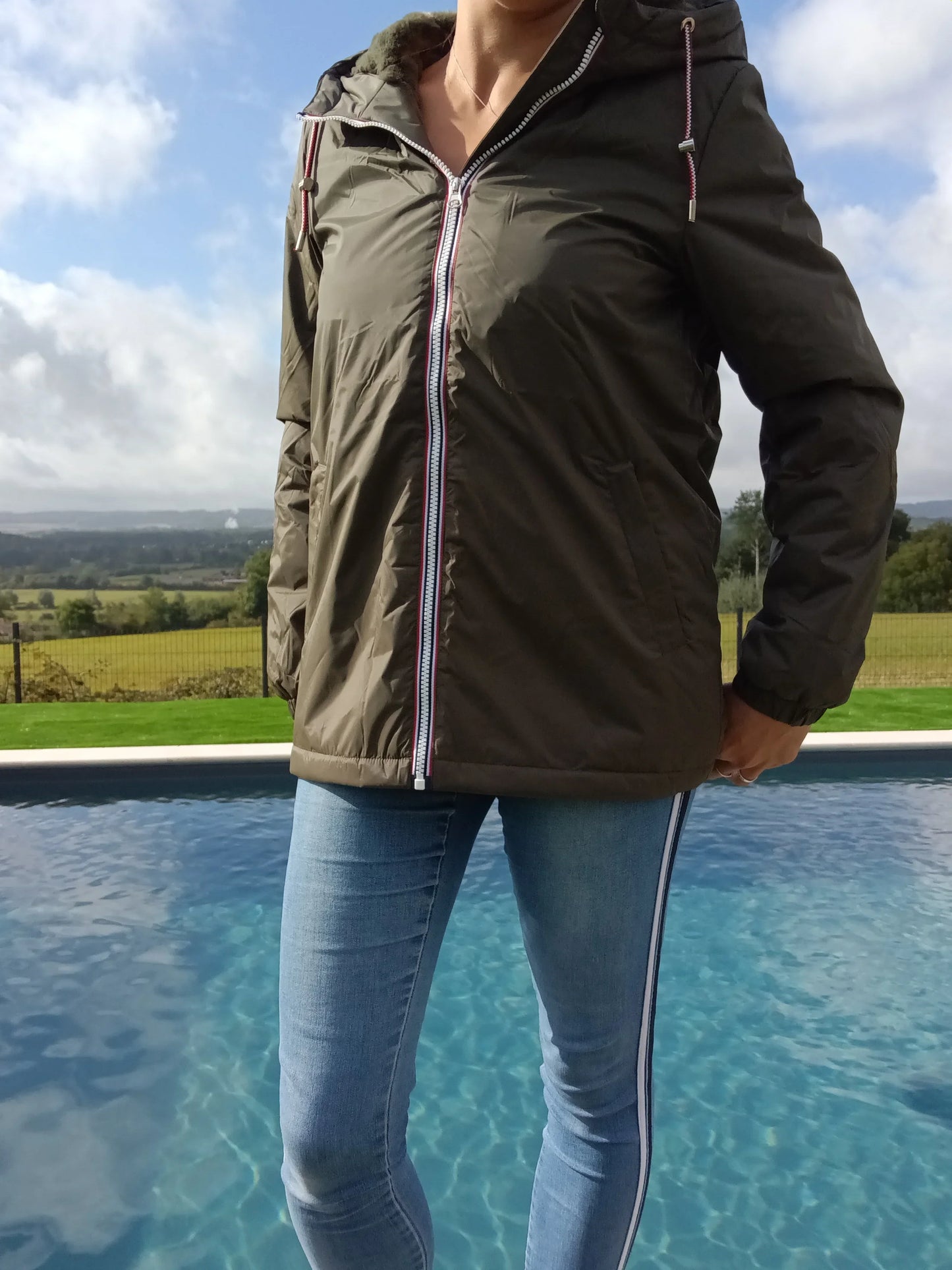 Woman in Laura Jo khaki rain jacket and skinny jeans by a pool, Le Petit Placard outdoor fashion