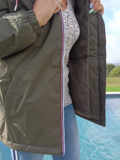 Woman in green Laura Jo raincoat with furry lining, floral top, and jeans by a pool outdoors