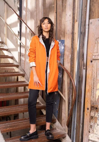 Woman wearing orange Laura Jo reversible raincoat, black top and jeans, Le Petit Placard