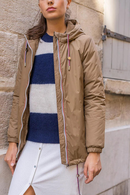 Woman wearing camel Laura Jo raincoat with tricolor drawstring, blue striped sweater, outside.
