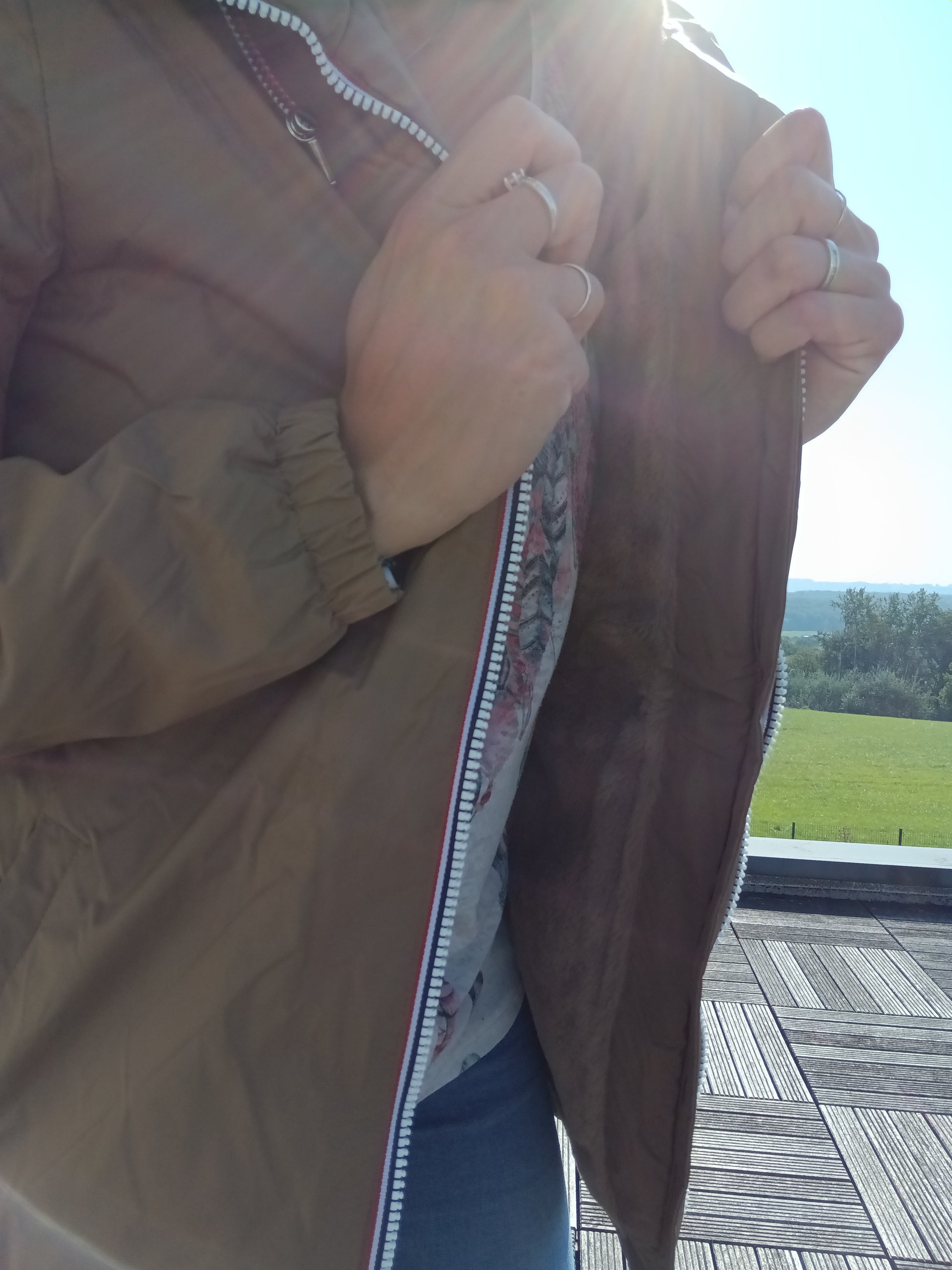 Person holding open camel Laura Jo raincoat with soft lining, outdoors in sunlight at Le Petit Placard