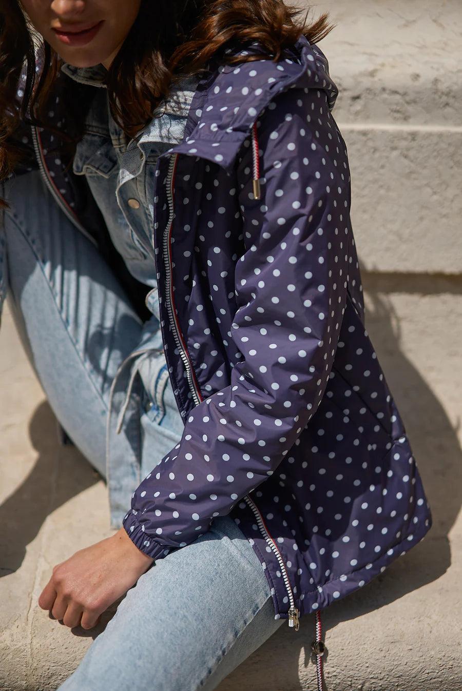 Woman wearing Laura Jo navy blue polka dot raincoat and denim on stone steps, Le Petit Placard