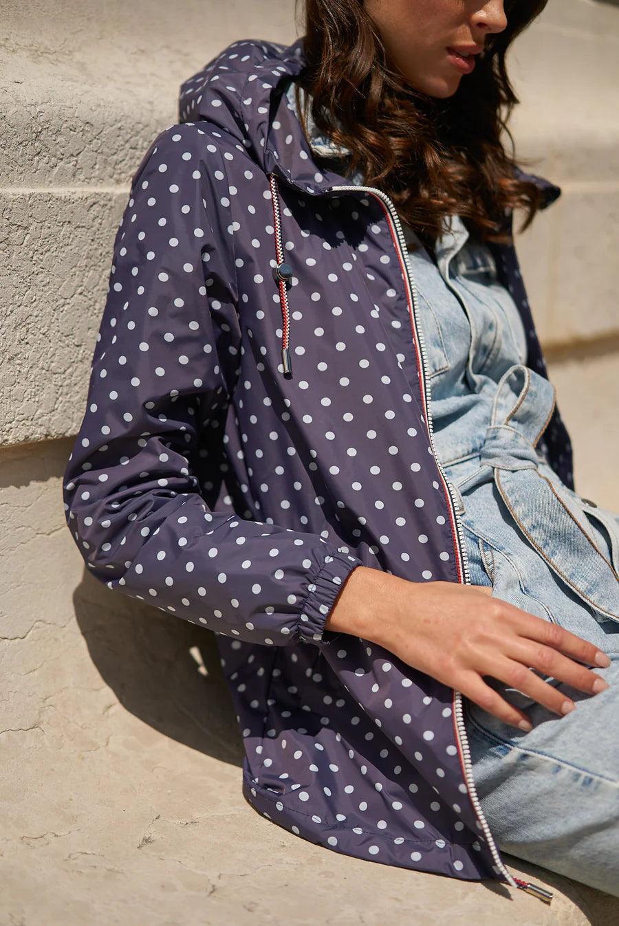 Woman wearing a navy blue polka dot Laura Jo raincoat from Le Petit Placard, seated outdoors