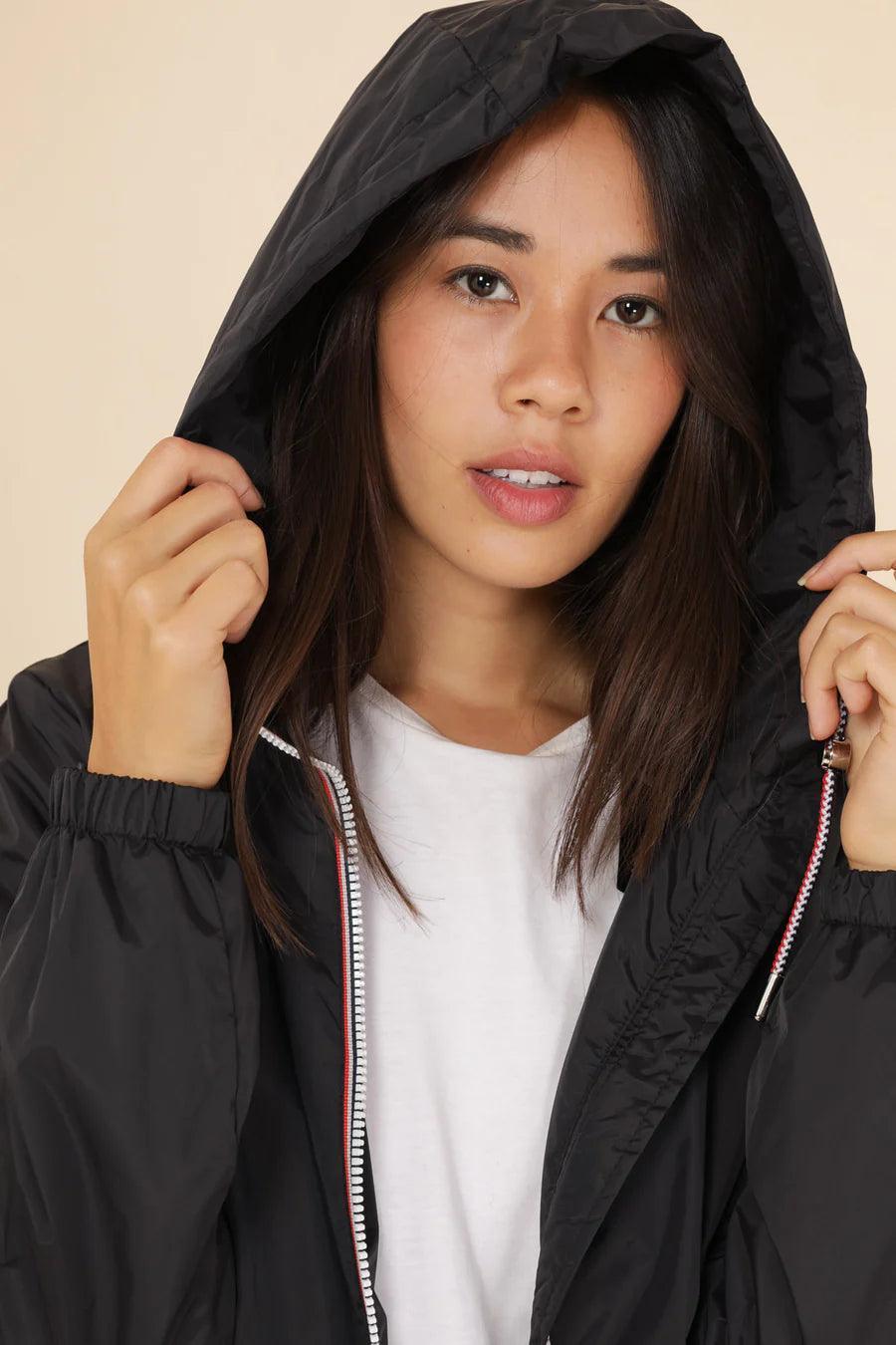 Woman wearing black Laura Jo raincoat with hood, featured at Le Petit Placard.