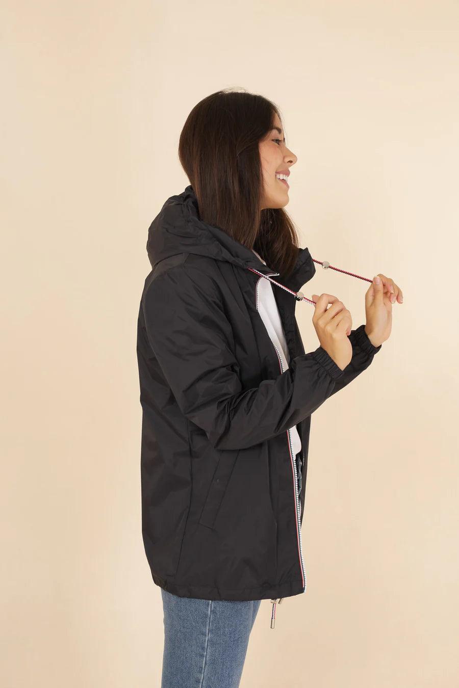 Woman wearing black Laura Jo raincoat from Le Petit Placard, side view, beige background