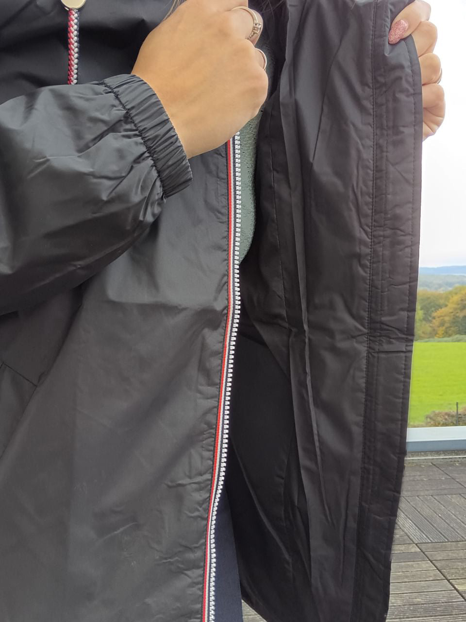 Close-up of person zipping a black Laura Jo raincoat outdoors, Le Petit Placard