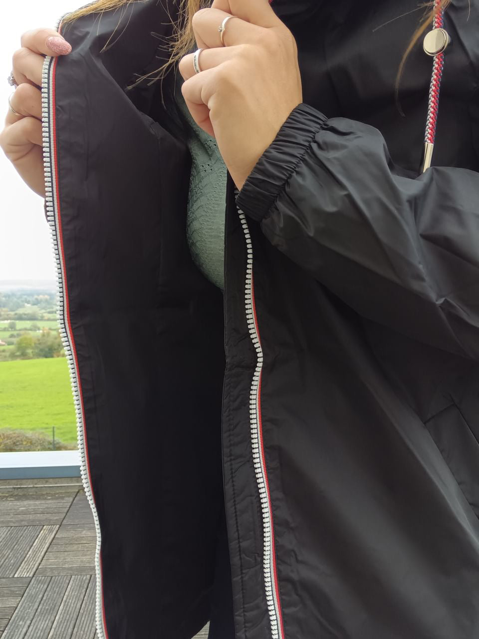 Close-up of Laura Jo black raincoat with red-accented zipper, shown outdoors at Le Petit Placard.