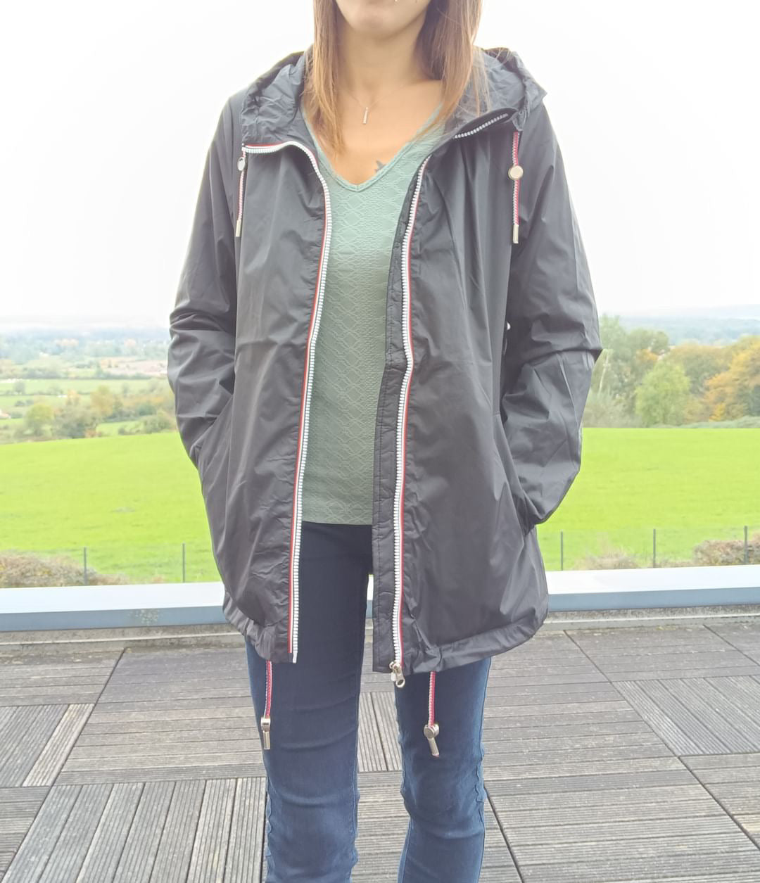 Woman wearing Laura Jo black rain jacket, standing outdoors on wooden terrace, Le Petit Placard
