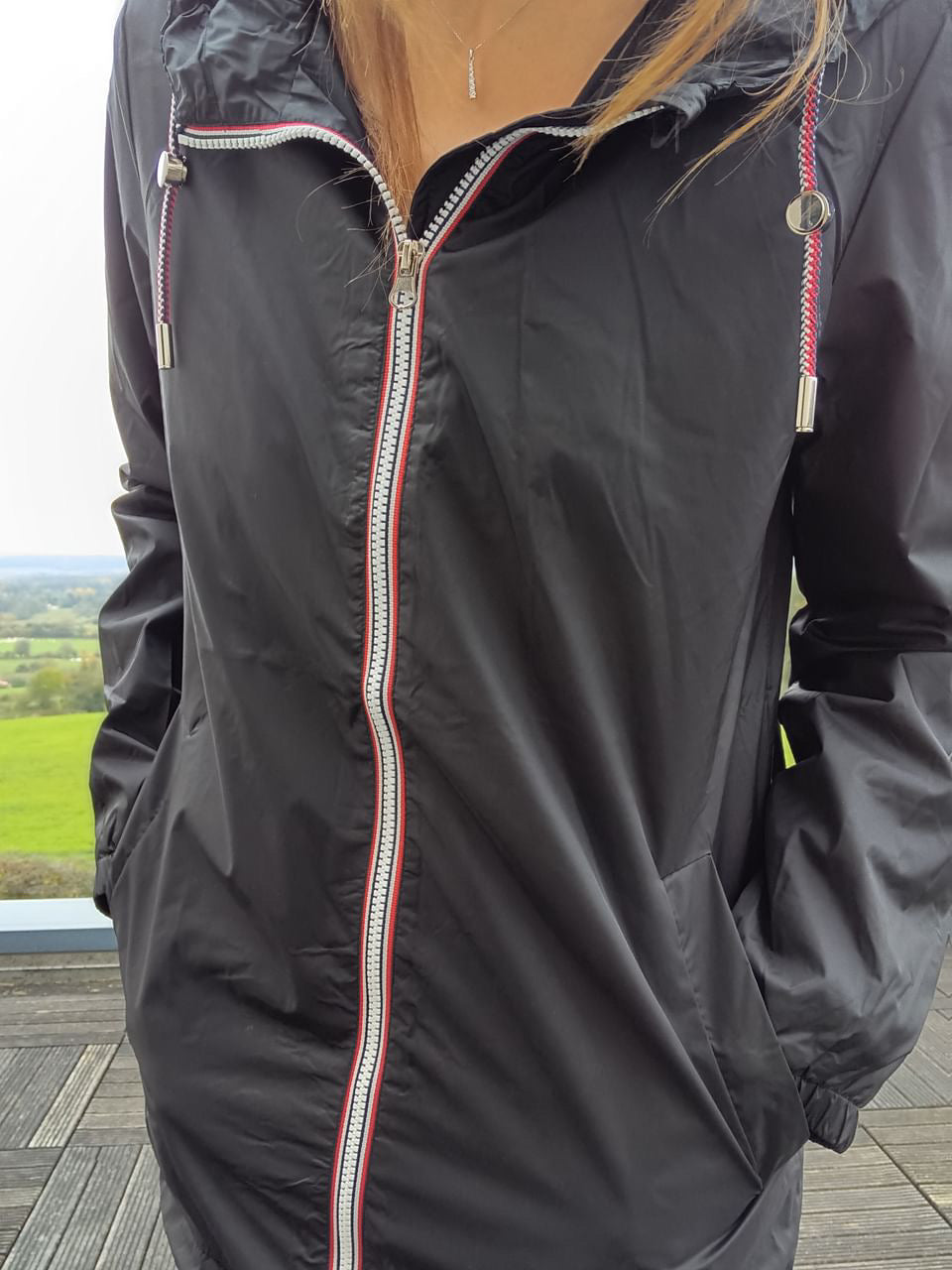Woman in a black Laura Jo raincoat with red-trimmed zipper outdoors, Le Petit Placard