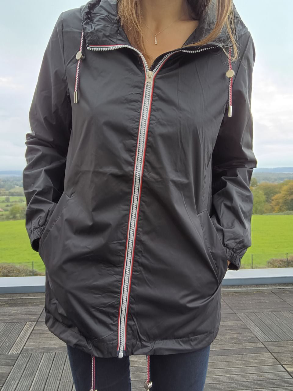 Woman wearing black Laura Jo mid-length raincoat with hood, outdoors, Le Petit Placard