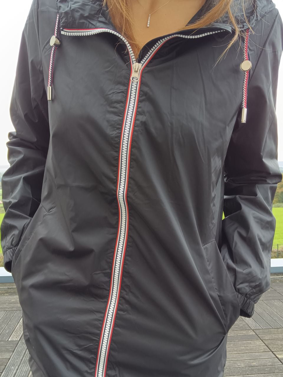 Black Laura Jo mid-length raincoat with red-trimmed zipper, outdoor setting, Le Petit Placard