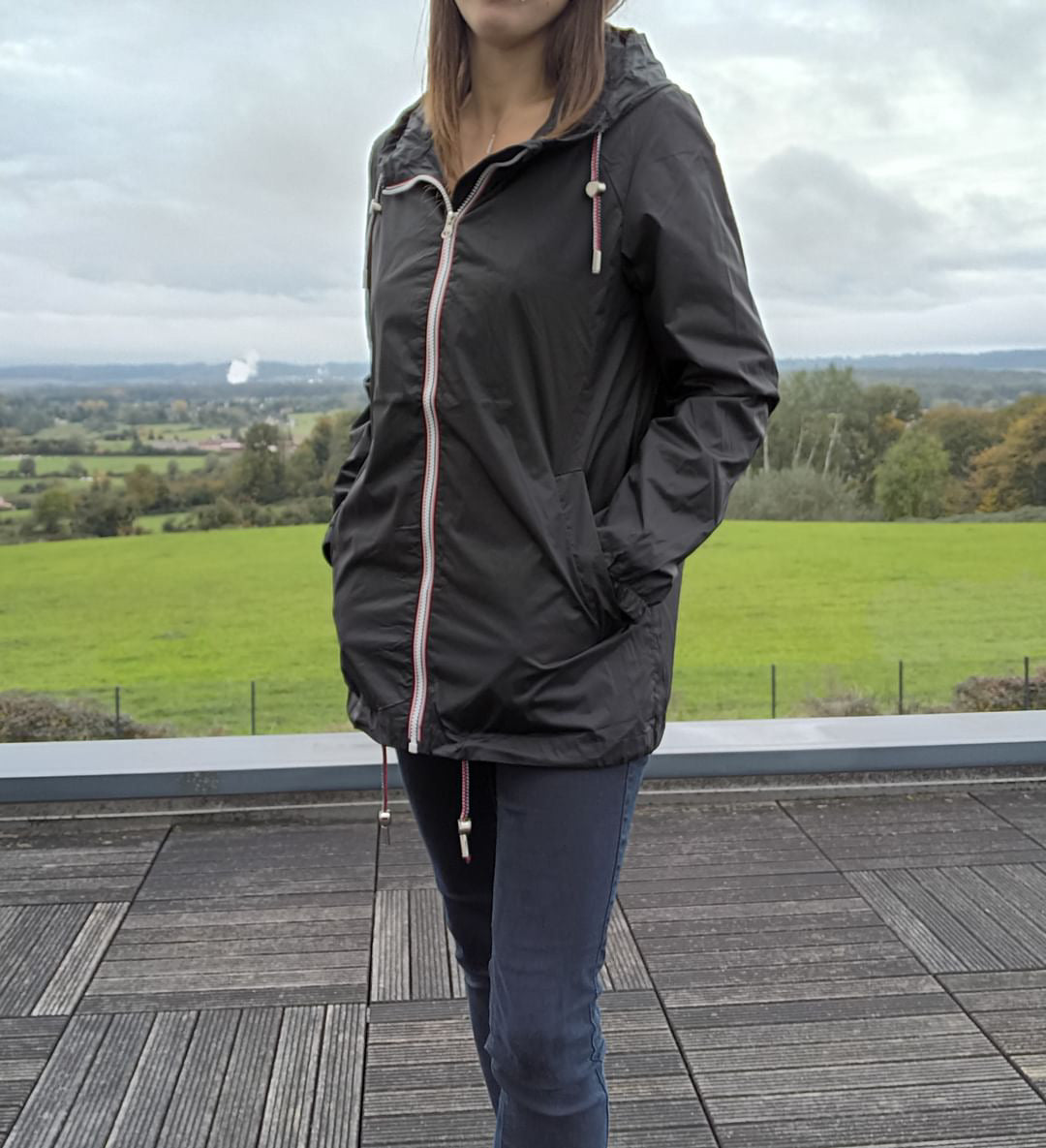 Woman wearing Laura Jo black raincoat on terrace with scenic countryside background