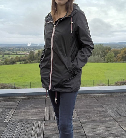 Woman wearing Laura Jo black raincoat on terrace with scenic countryside background