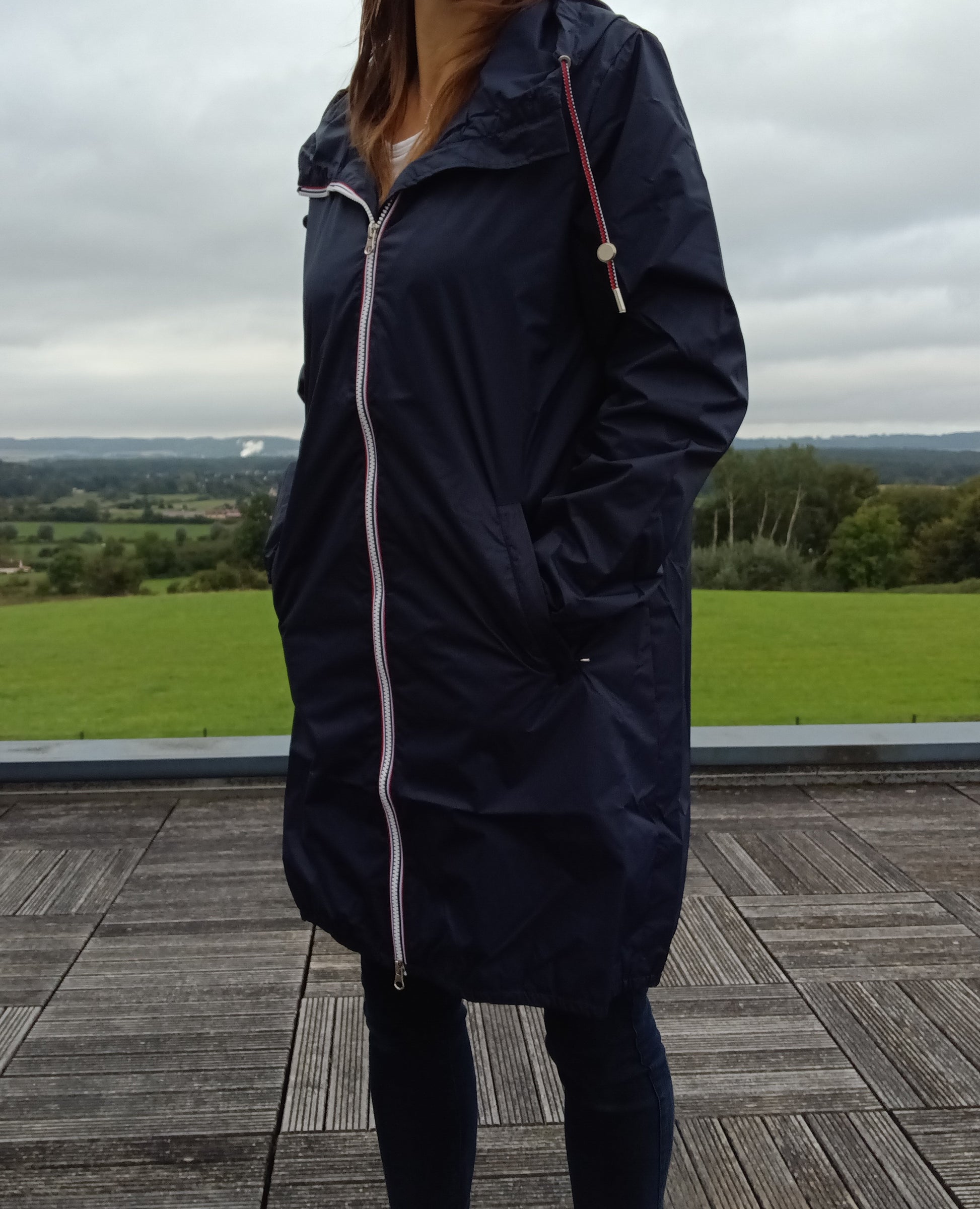 Femme portant le parka manteau long bleu marine imperméable Laura Jo avec capuche et zip tricolore, en extérieur