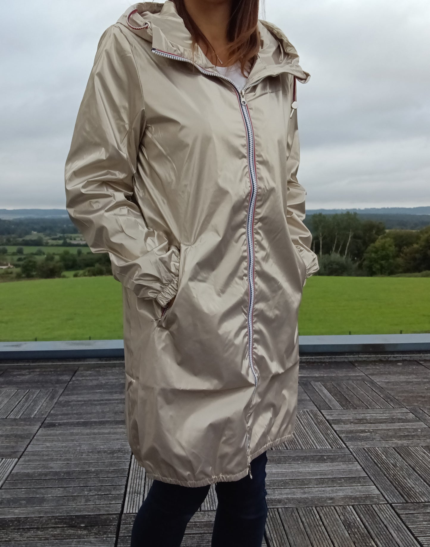Parka manteau long imperméable doré Laura Jo à capuche et zip tricolore, porté par une femme en extérieur