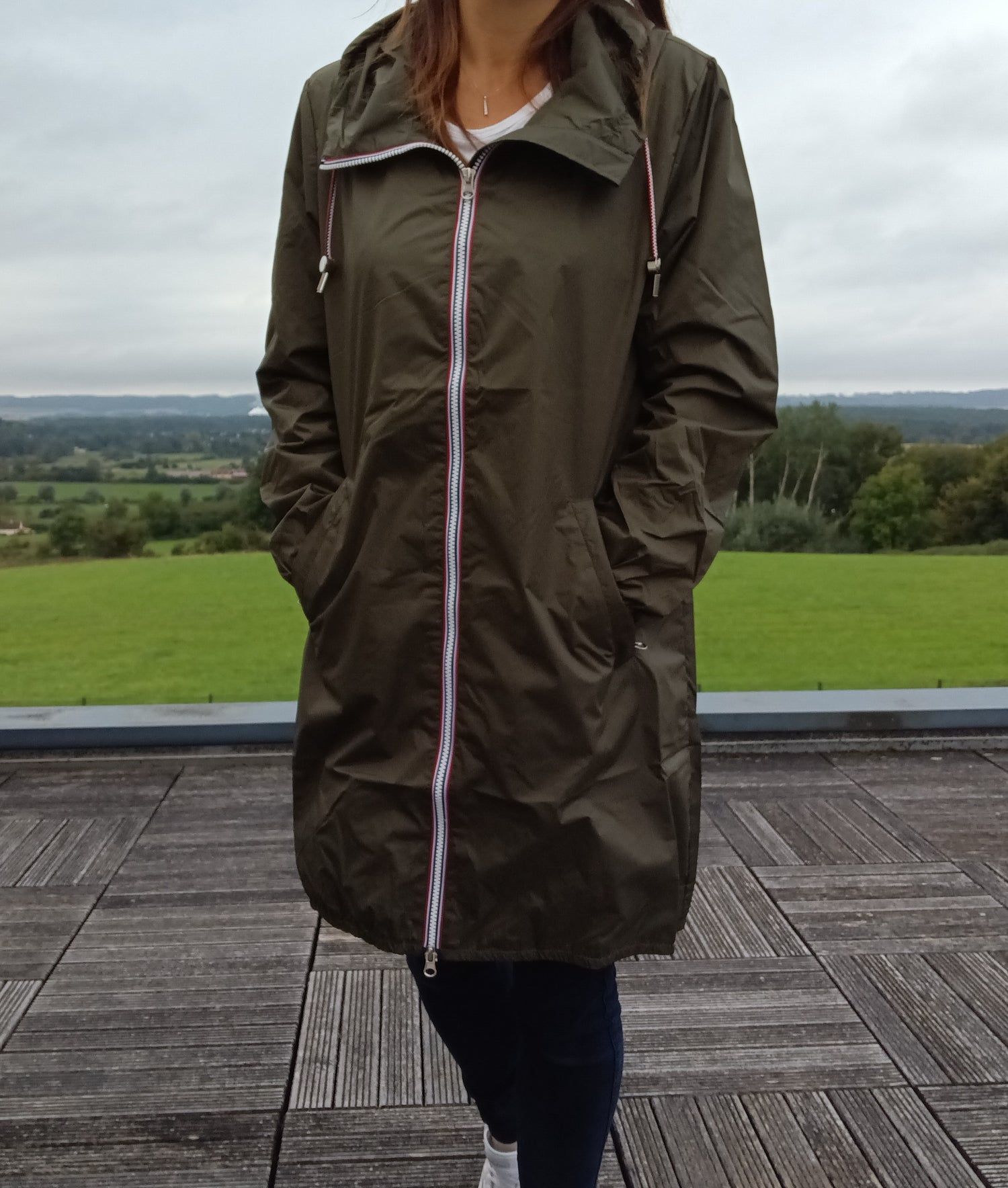 Woman wearing Laura Jo khaki raincoat with zipper, standing on terrace, outdoor view