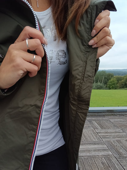 Woman wearing khaki Laura Jo raincoat outdoors, opening jacket to show white t-shirt