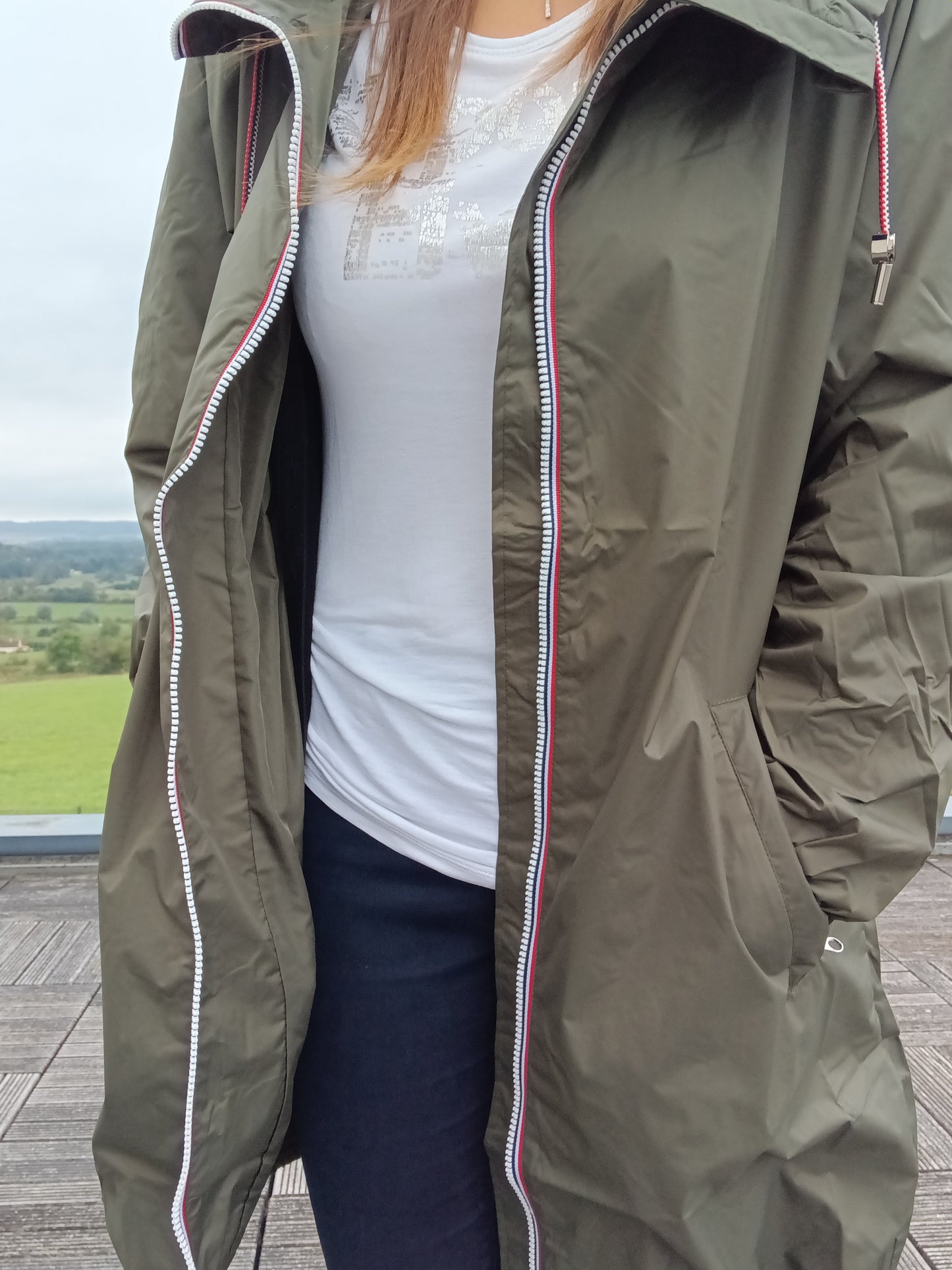 Woman wearing khaki Laura Jo raincoat, white t-shirt, outdoors at Le Petit Placard