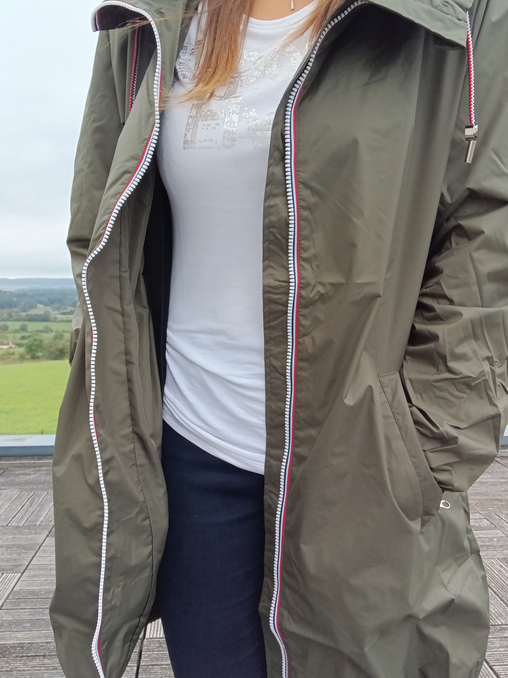 Woman wearing khaki Laura Jo raincoat, white t-shirt, outdoors at Le Petit Placard
