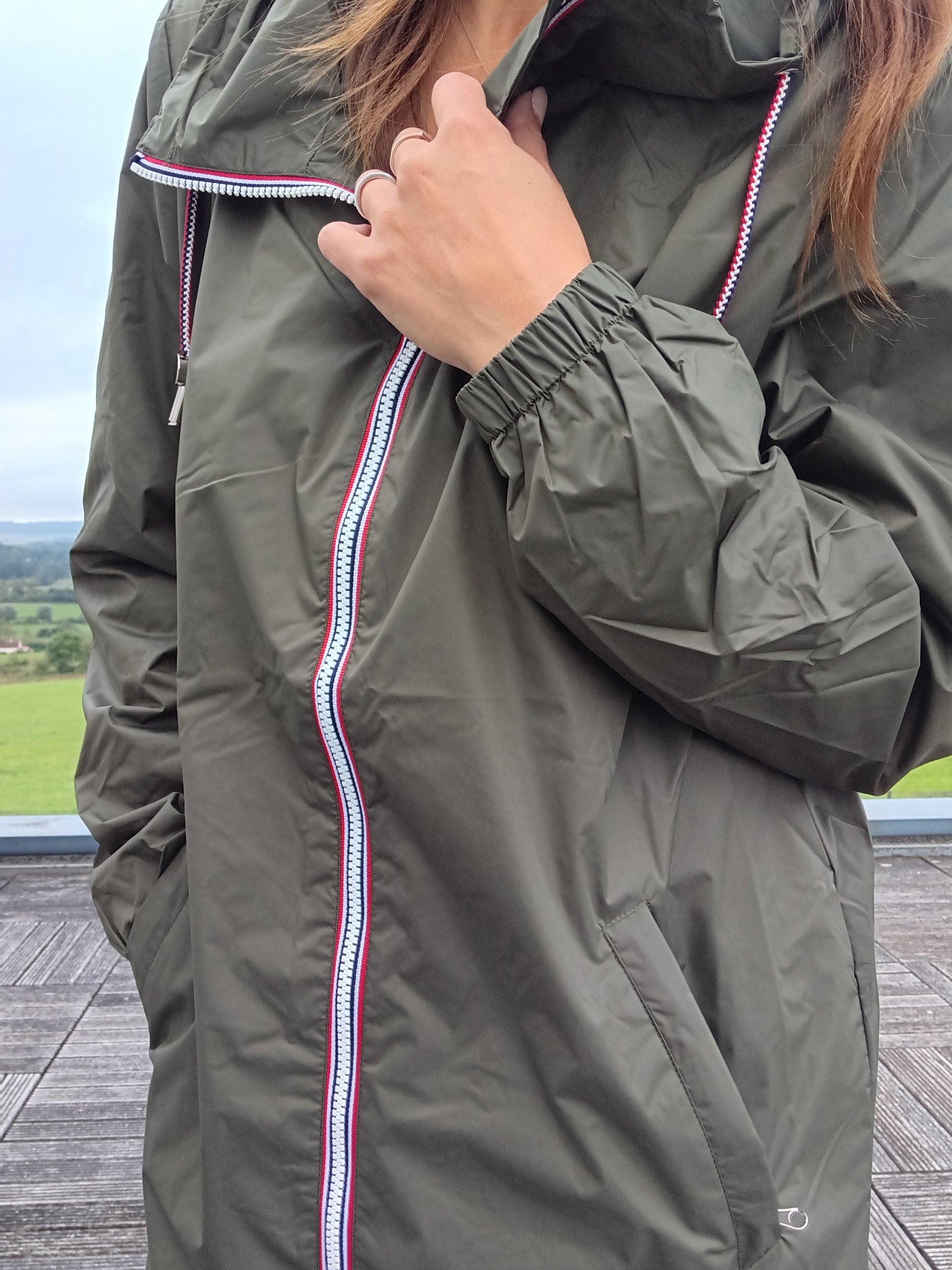 Woman wearing khaki Laura Jo raincoat with striped zipper outdoors, Le Petit Placard