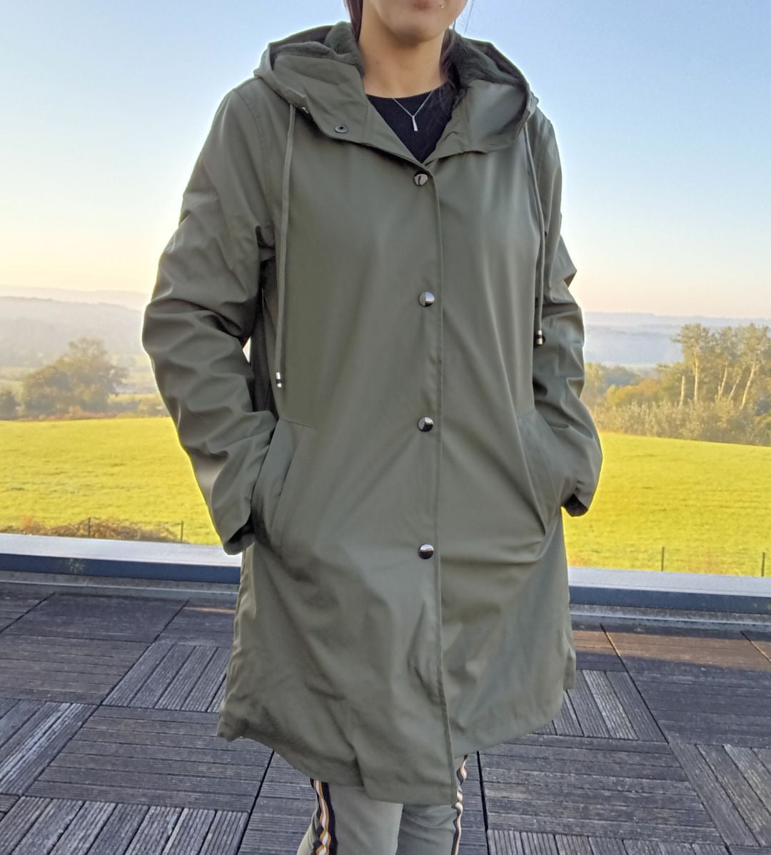 Woman wearing long khaki waterproof raincoat with hood outdoors, Le Petit Placard