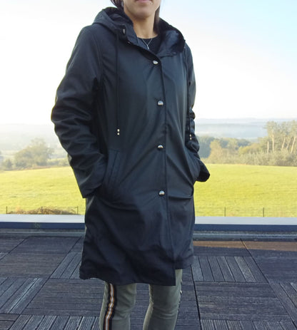 Woman wearing Laura Jo black raincoat from Le Petit Placard, outdoors on a terrace.