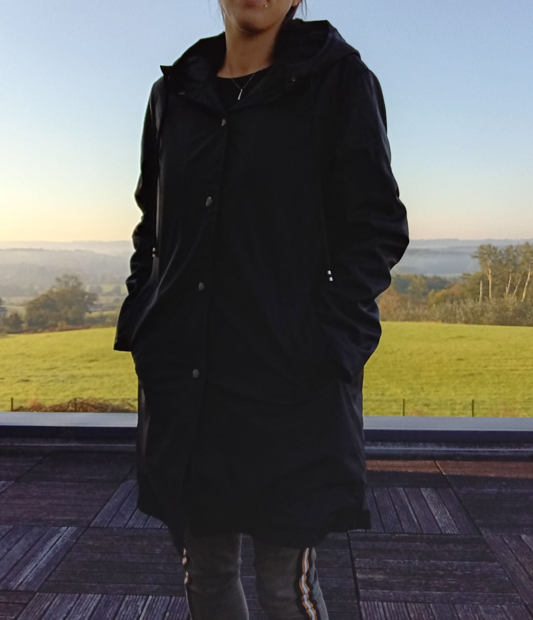 Woman wearing black Laura Jo raincoat outdoors, countryside background, Le Petit Placard
