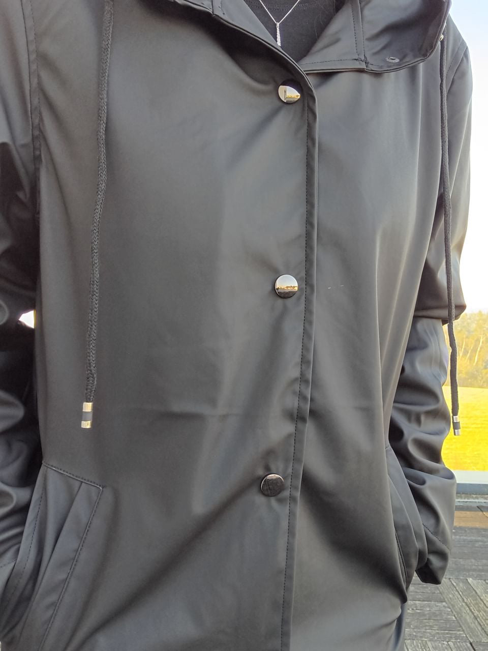 Black Laura Jo raincoat with hood and silver buttons from Le Petit Placard, outdoor setting