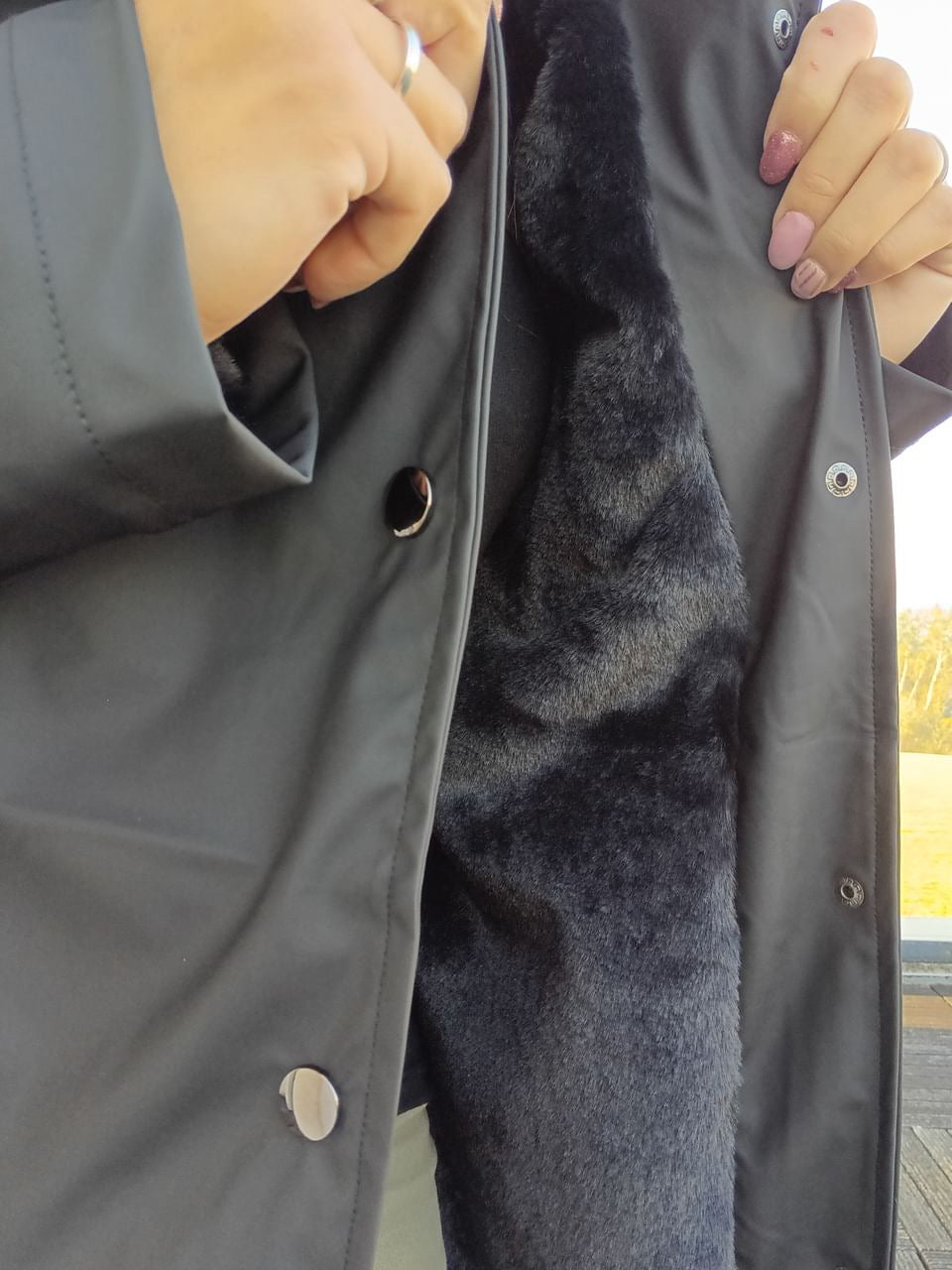 Black waterproof long coat with faux fur lining, shown open by hands, Le Petit Placard