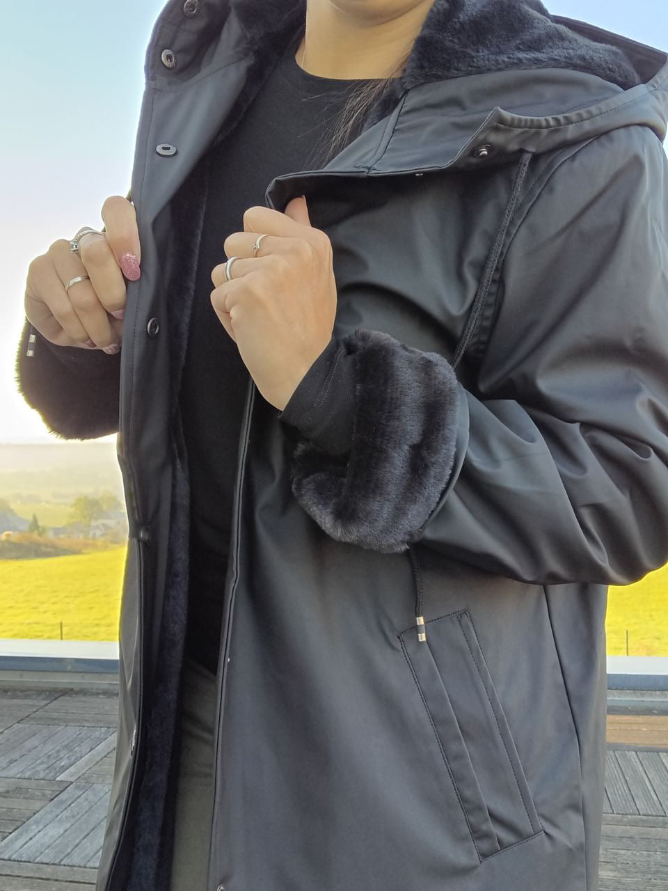 Woman wearing a long black waterproof faux fur-lined coat from Le Petit Placard outdoors