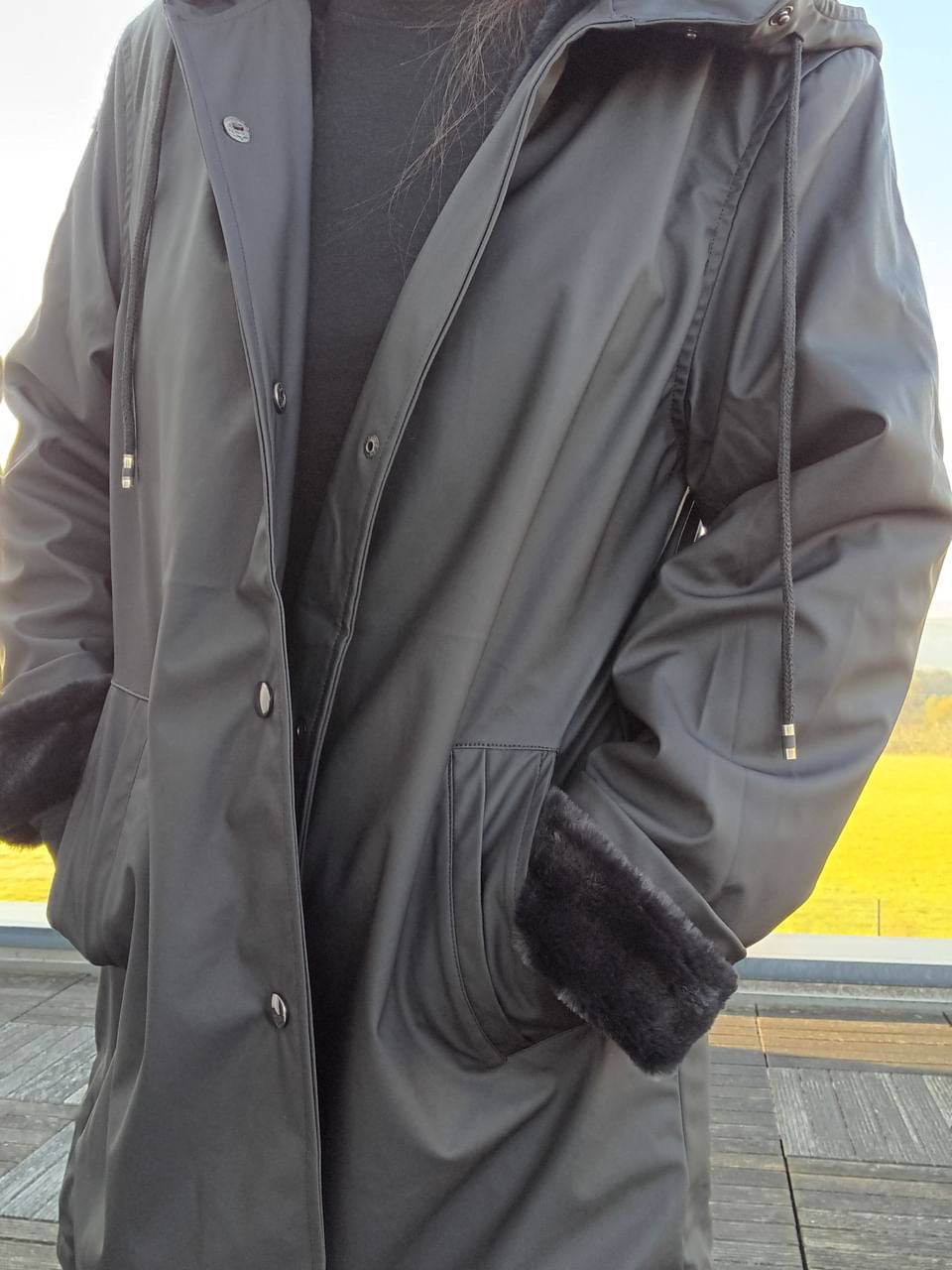 Black long waterproof Laura Jo raincoat with faux fur cuffs, outdoors, Le Petit Placard