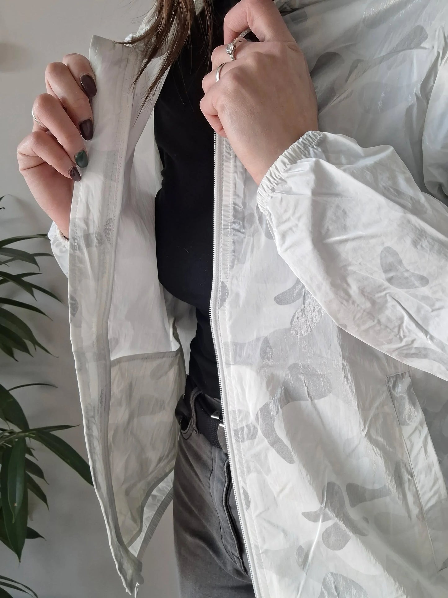 Woman wearing a white patterned Laura Jo raincoat, black top, grey jeans, Le Petit Placard