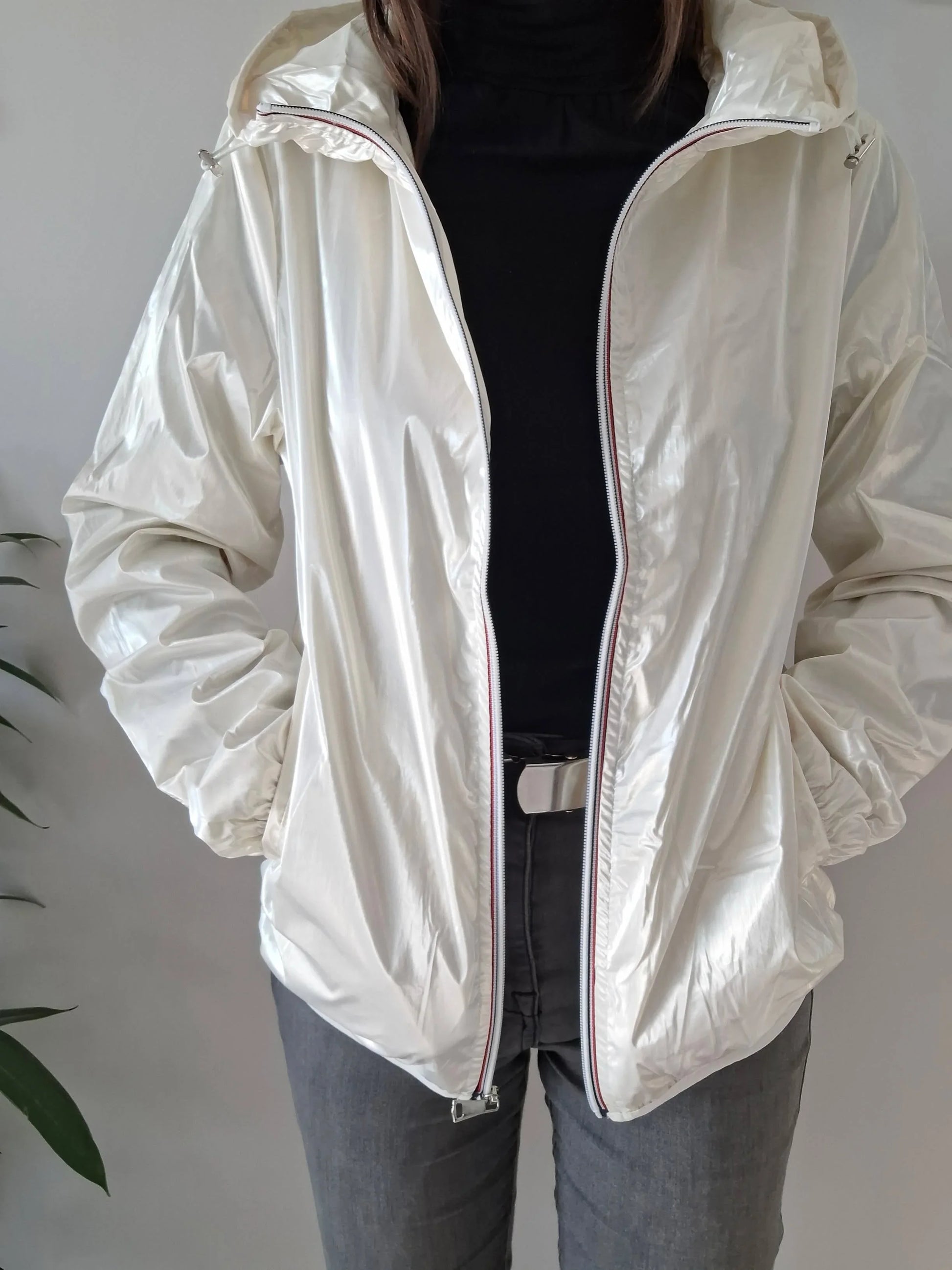 Woman wearing a shiny white Laura Jo raincoat, black top, and grey jeans from Le Petit Placard.
