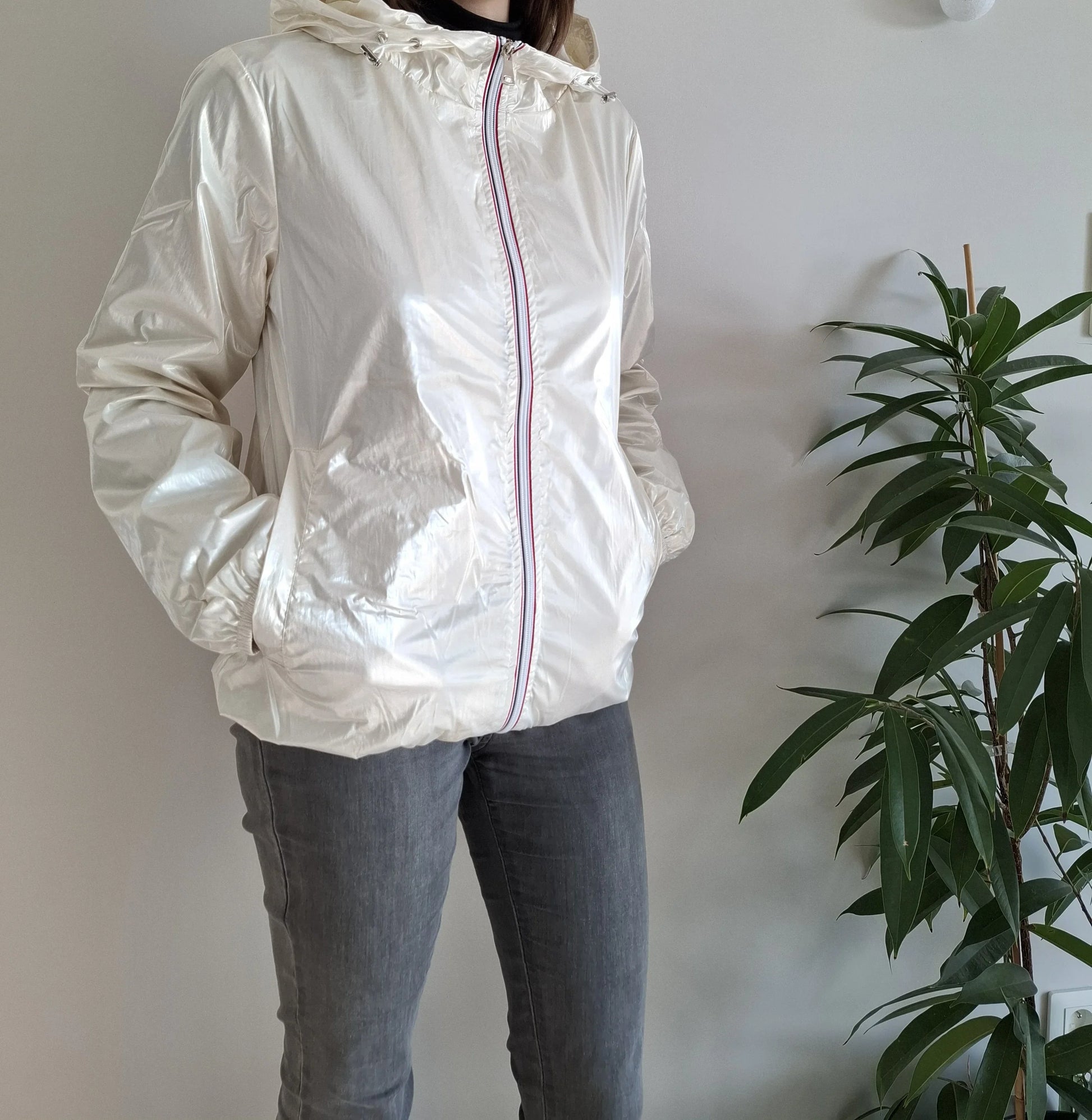 Woman wearing shiny white Laura Jo raincoat from Le Petit Placard, indoors by a green plant.