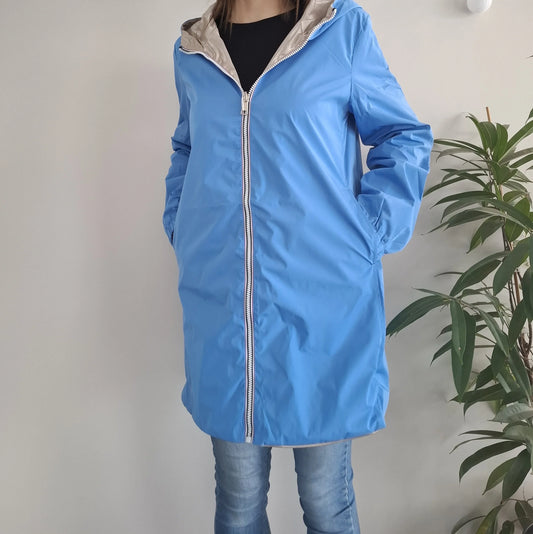 Manteau long réversible imperméable bleu porté par une femme, côté bleu visible avec capuche dorée et fermeture éclair