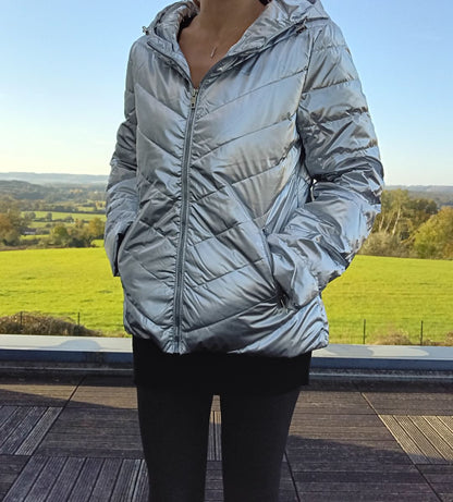 Woman wearing shiny silver Laura Jo puffer jacket outside on a terrace, green field view