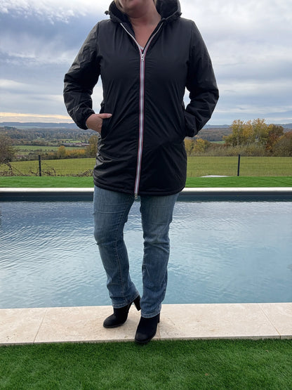 Femme portant une parka imperméable longue noire Laura Jo avec capuche et fermeture éclair, associée à un jean et bottines noires